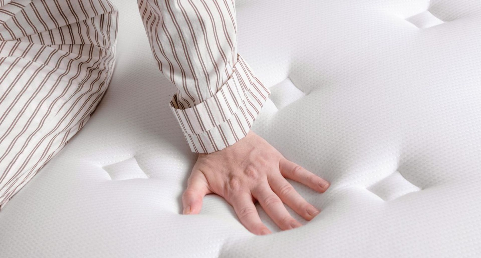 Close up of the surface of a mattress and a person pushing down on it