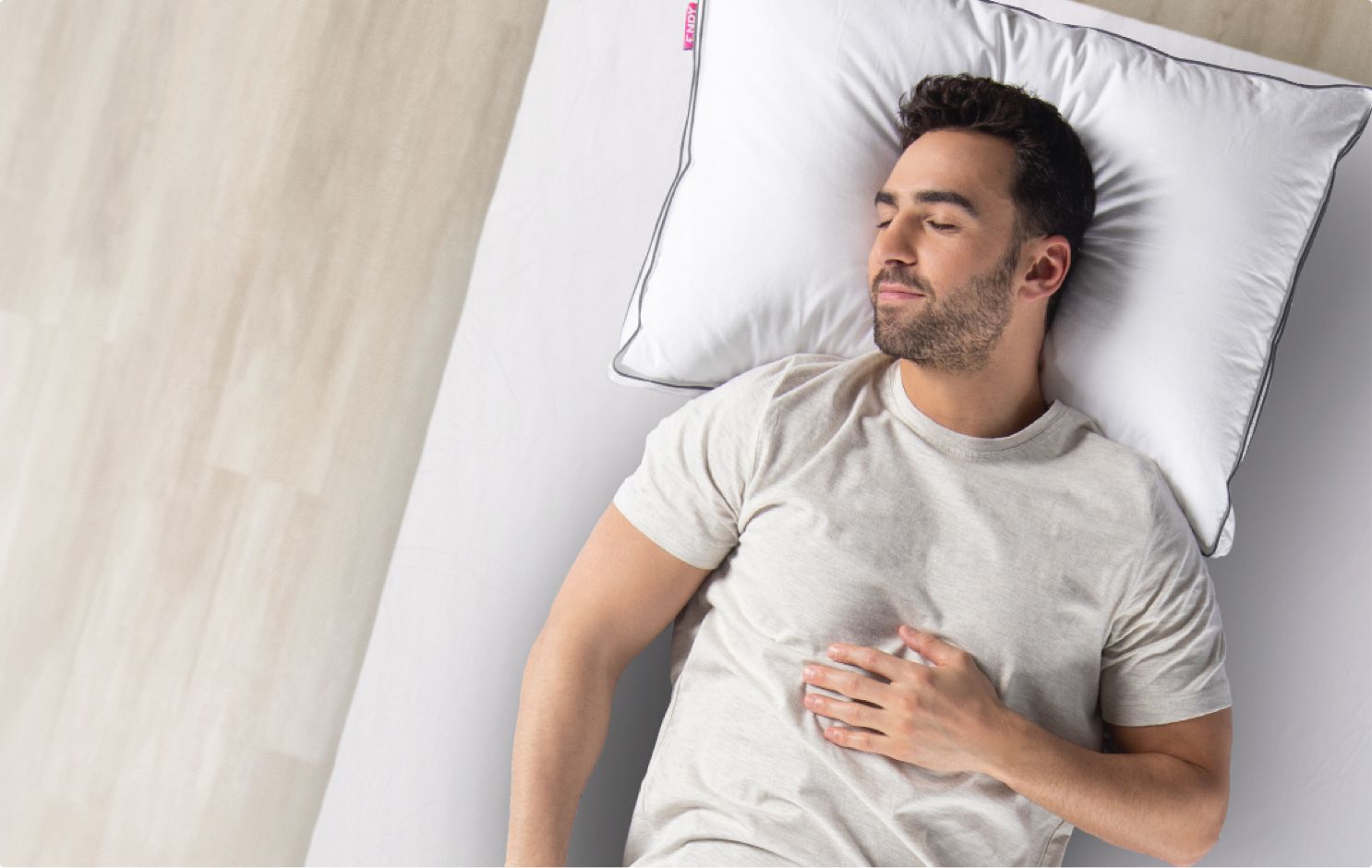 Man in a white t-shirt lying on a mattress with a plush pillow under his head