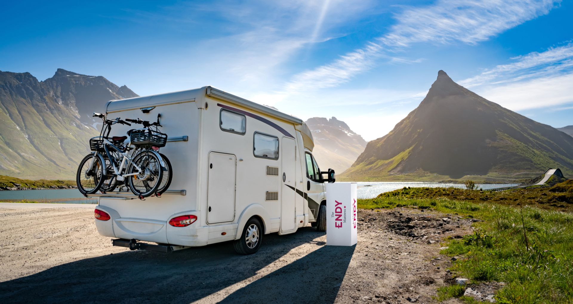 An Endy Mattress box beside a parked RV featuring a mountain landscape. 