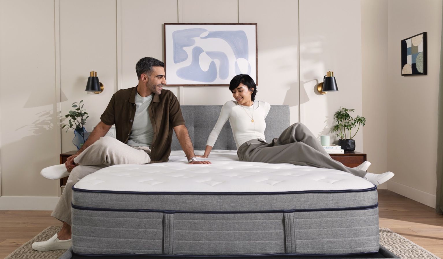 Man and woman sitting on an Endy Hybrid mattress on a grey bed frame