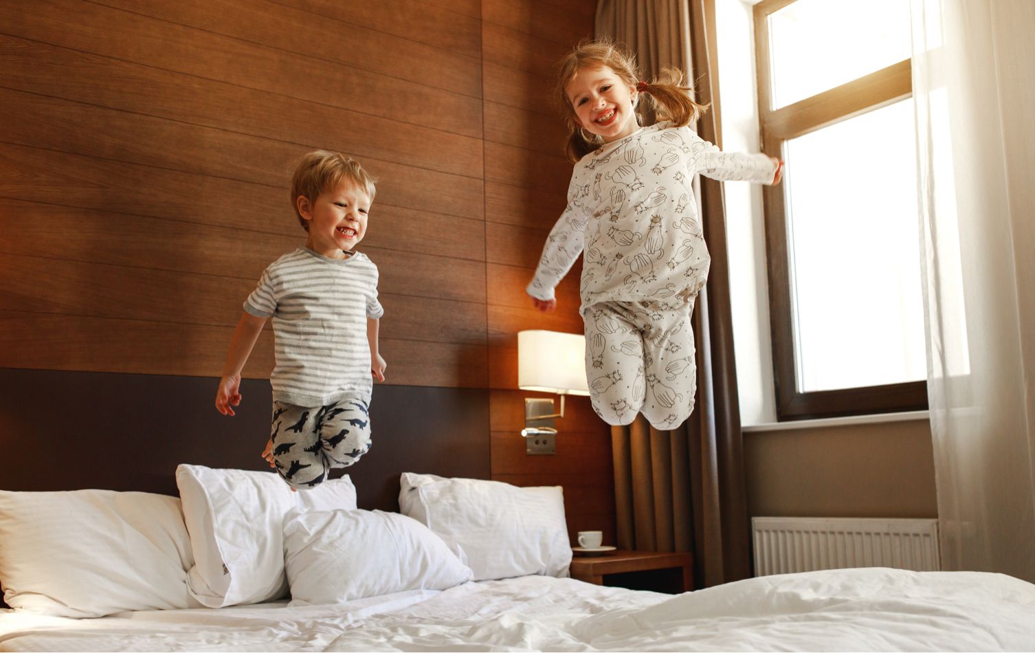 Two children happily jumping on a bed.