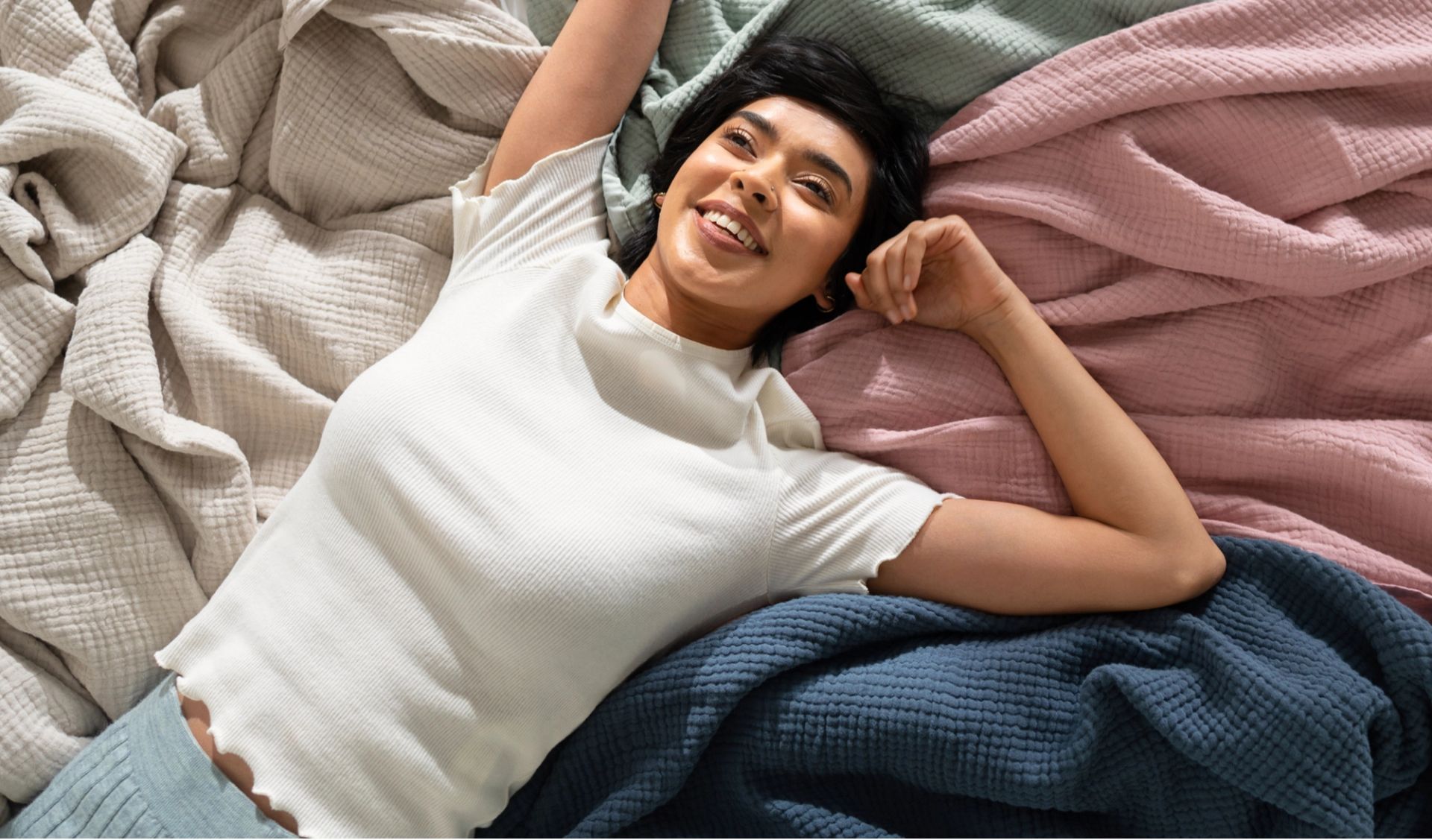 Woman lying on top of muslin blankets of various colours