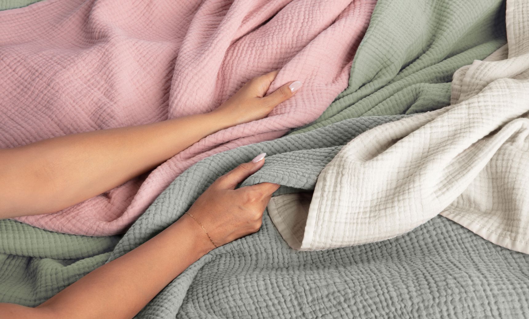 Various colours of Endy Muslin Blankets draped together, hands running over them