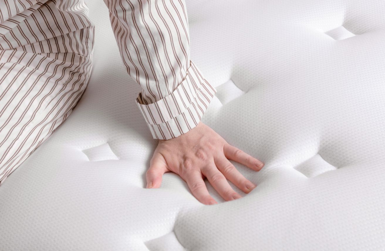 Person sitting on Endy Mattress pressing hand into top layer to demonstrate firmness.