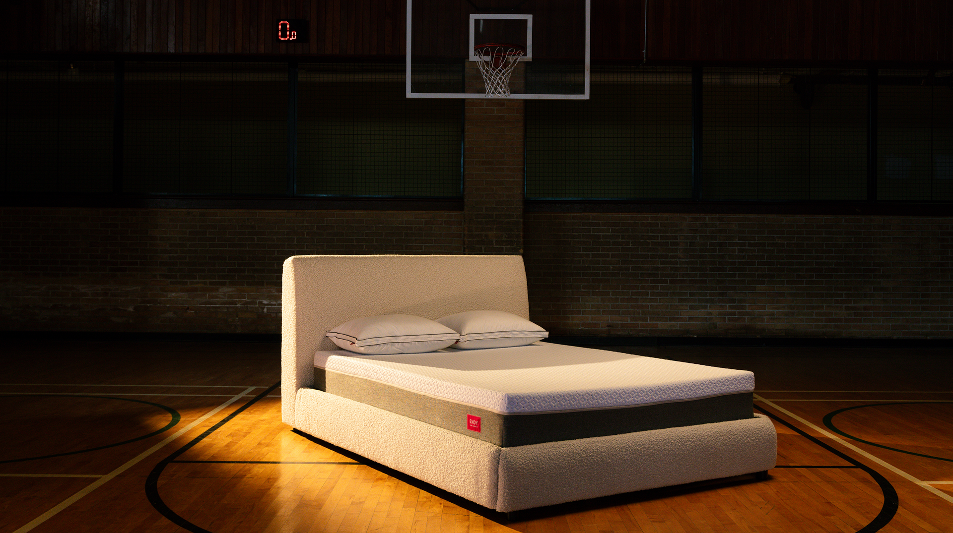Bare Endy Mattress on a white Upholstered bed frame, sitting on a basketball court