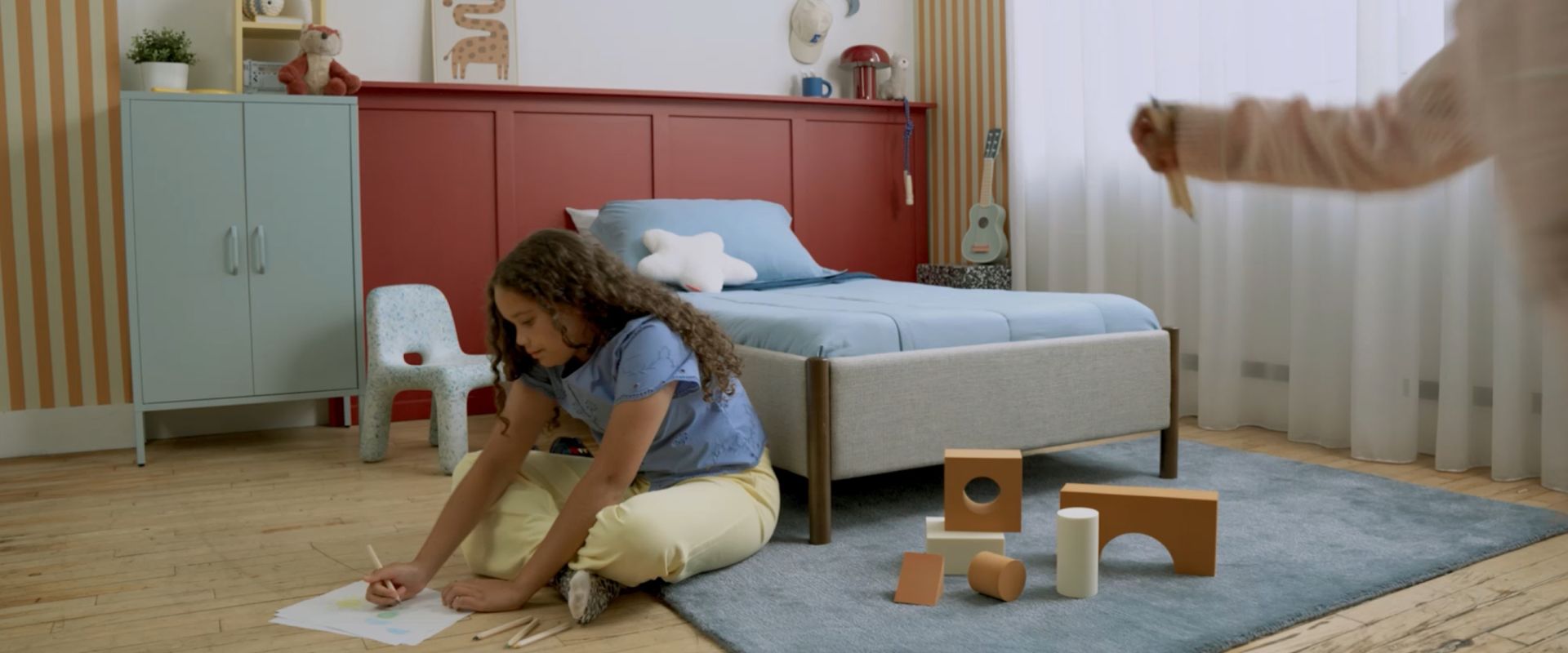 Pre-teen girl draws on the floor in a bedroom with an Endy Petit mattress behind her