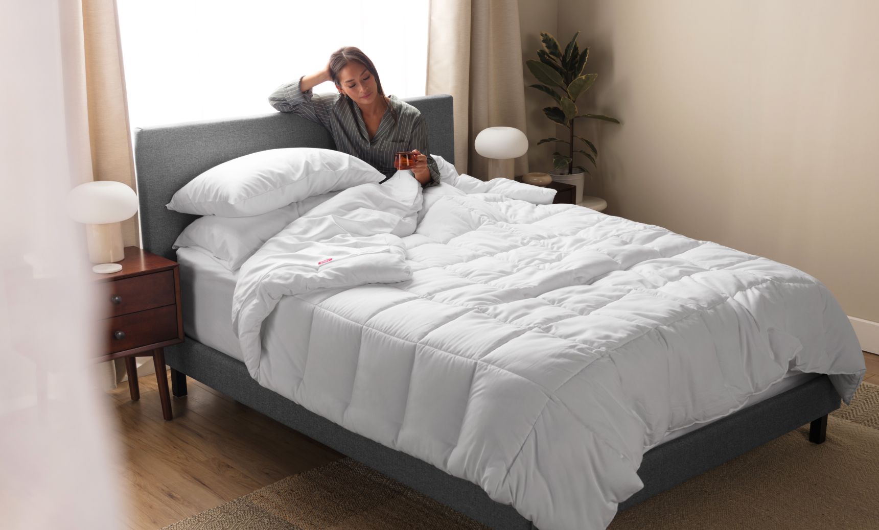 Woman sitting up in an Endy Upholstered bed under a white Endy Duvet