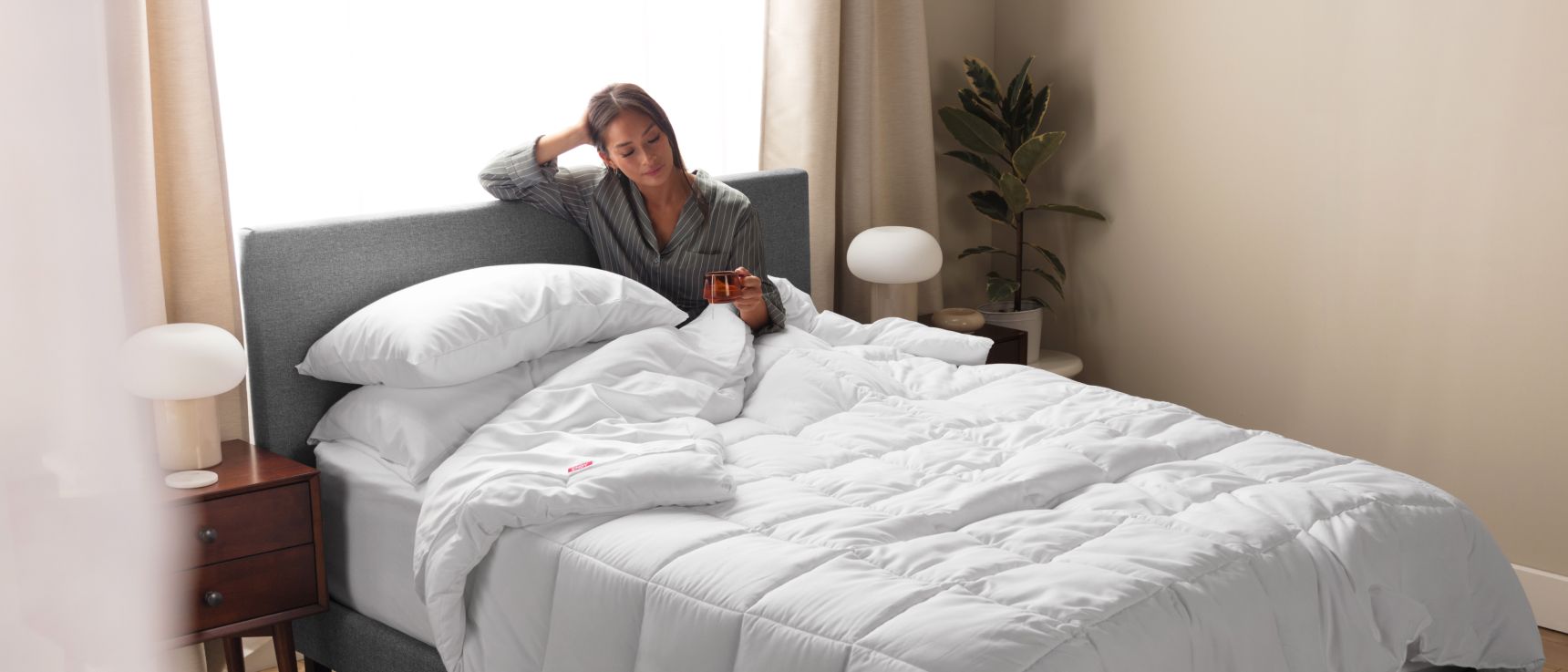 Woman sitting up in an Endy Upholstered bed under a white Endy Duvet