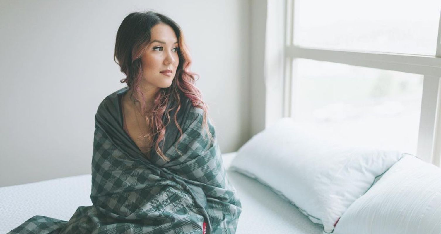 Image of a woman sitting up in bed, wrapped in an Endy Weighted Blanket