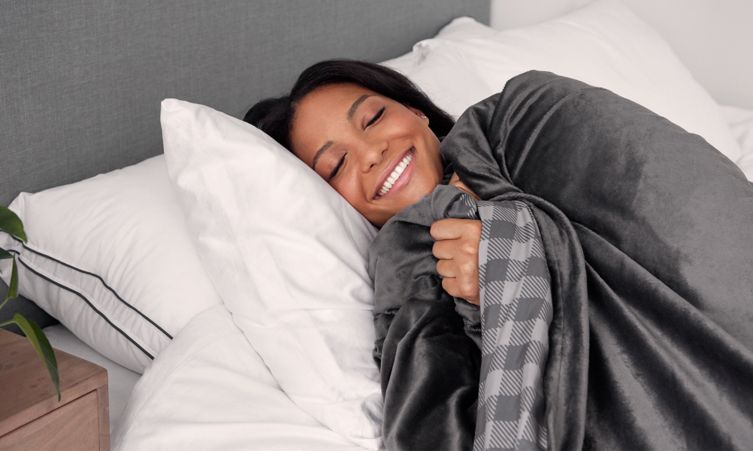 A person laying down in bed with a smile, snug under an Endy Weighted Blanket.