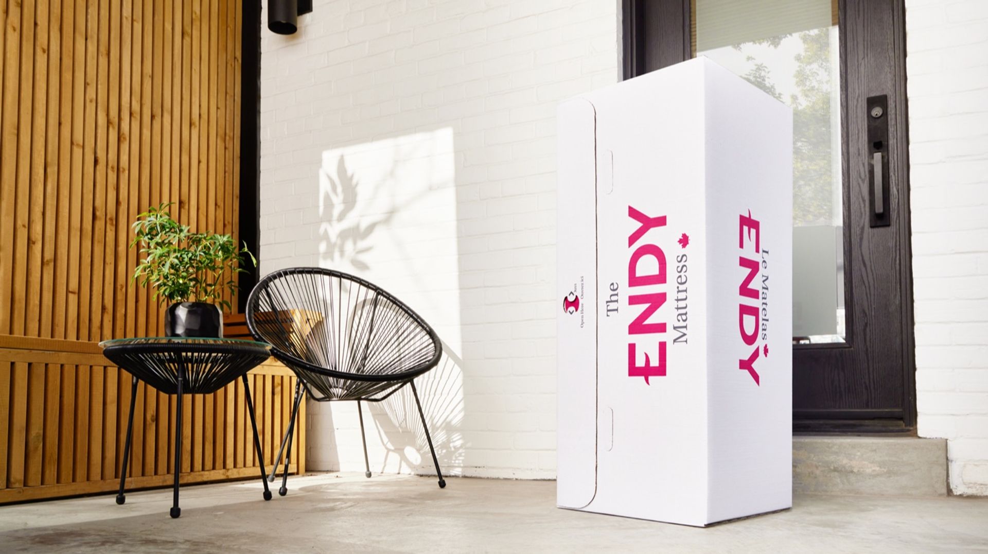 An Endy box stands upright on the porch of a white brick house in front of a black door