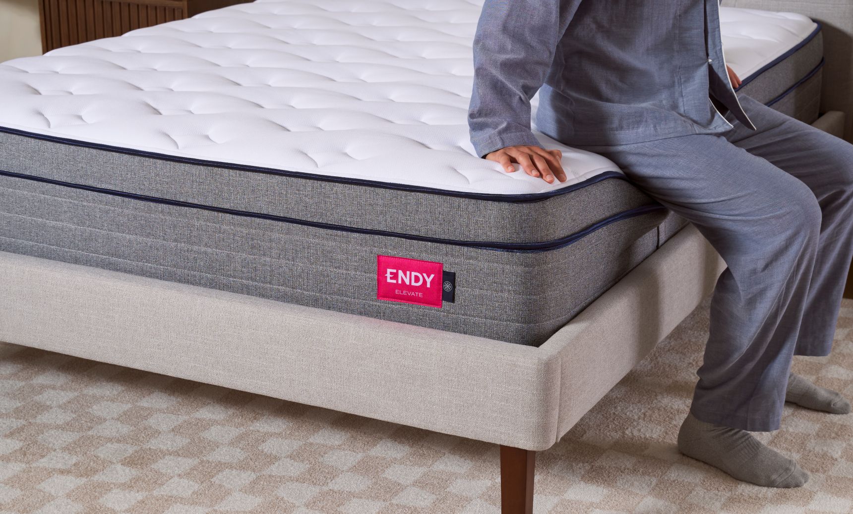 Person sitting on the edge of the Endy Elevate Hybrid Mattress to demonstrate construction.
