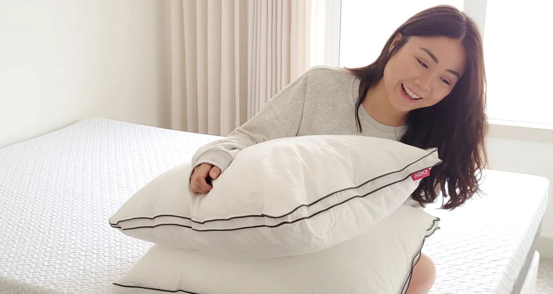  A woman sitting on her Endy Mattress and looking at her Endy Customizable Pillows