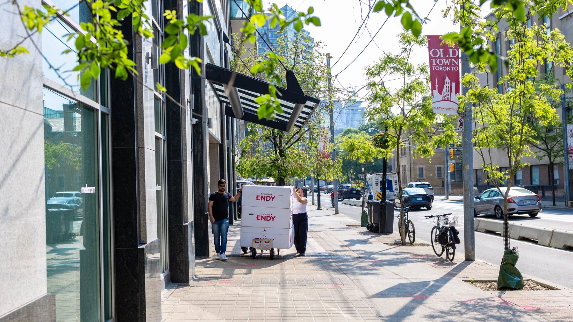 Two people rolling Endy mattresses on a dolly down the street in Toronto