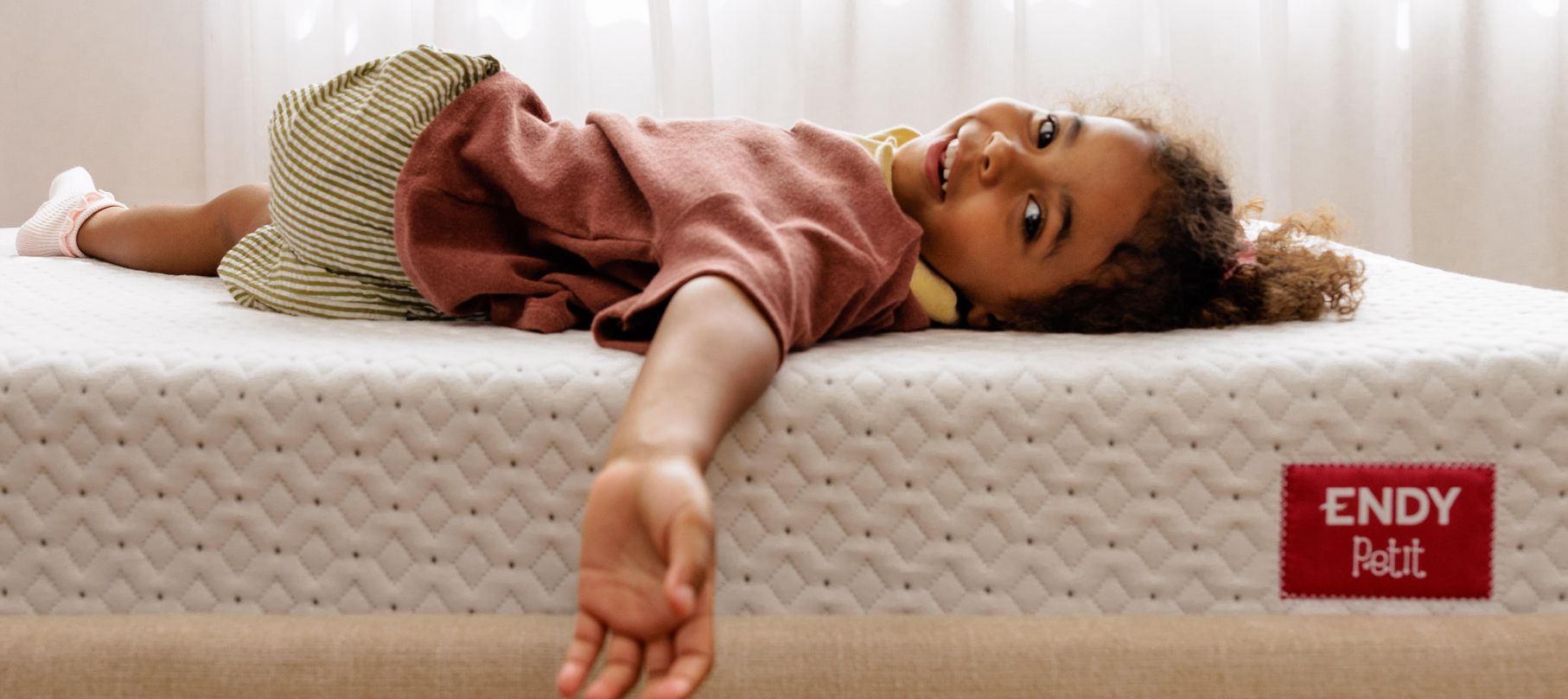 A smiling girl laying on an Endy Petit mattress