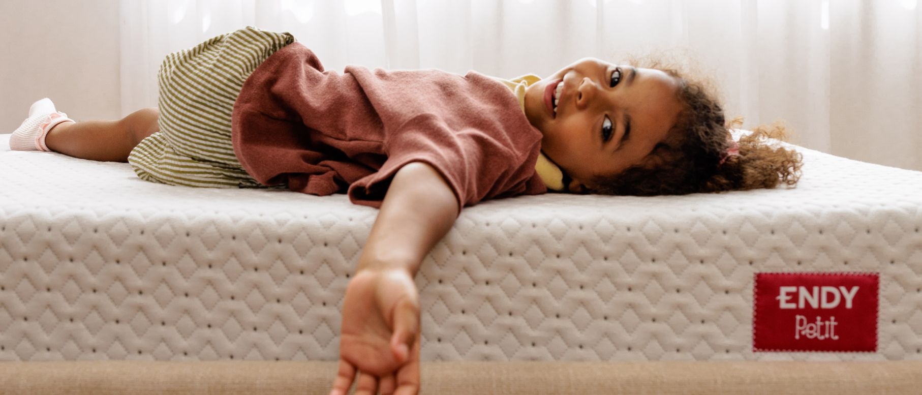 A smiling girl laying on an Endy Petit mattress