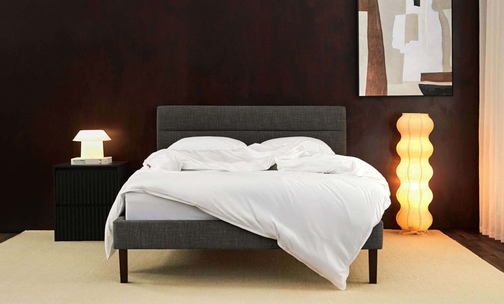 Bedroom with channel upholstered bed frame in graphite colourway, shown with wooden nightstand and soft cream sheets.