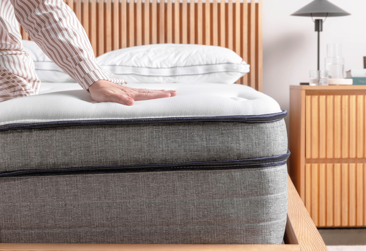 Close up shot of the corner of a bare Endy Hybrid mattress, a person's arm comes in from the left side of the frame to feel the mattress