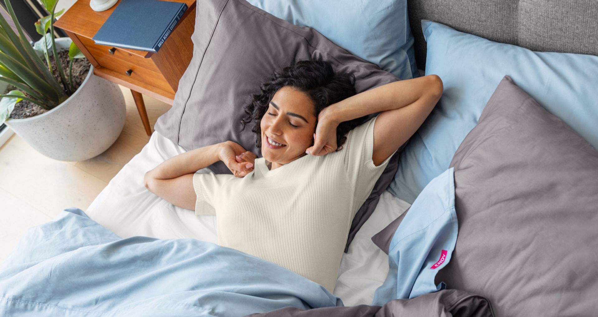 A woman lying in bed, stretching her arms as she wakes up.