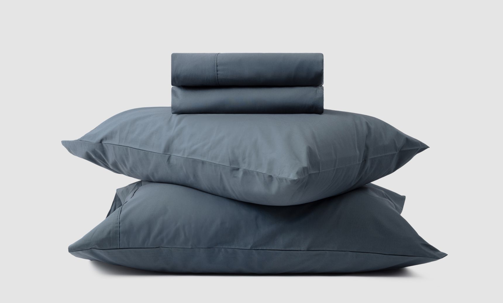 2 pillows stacked on top of each other, with a folded sheet resting on top, all of them are a dark blue colour