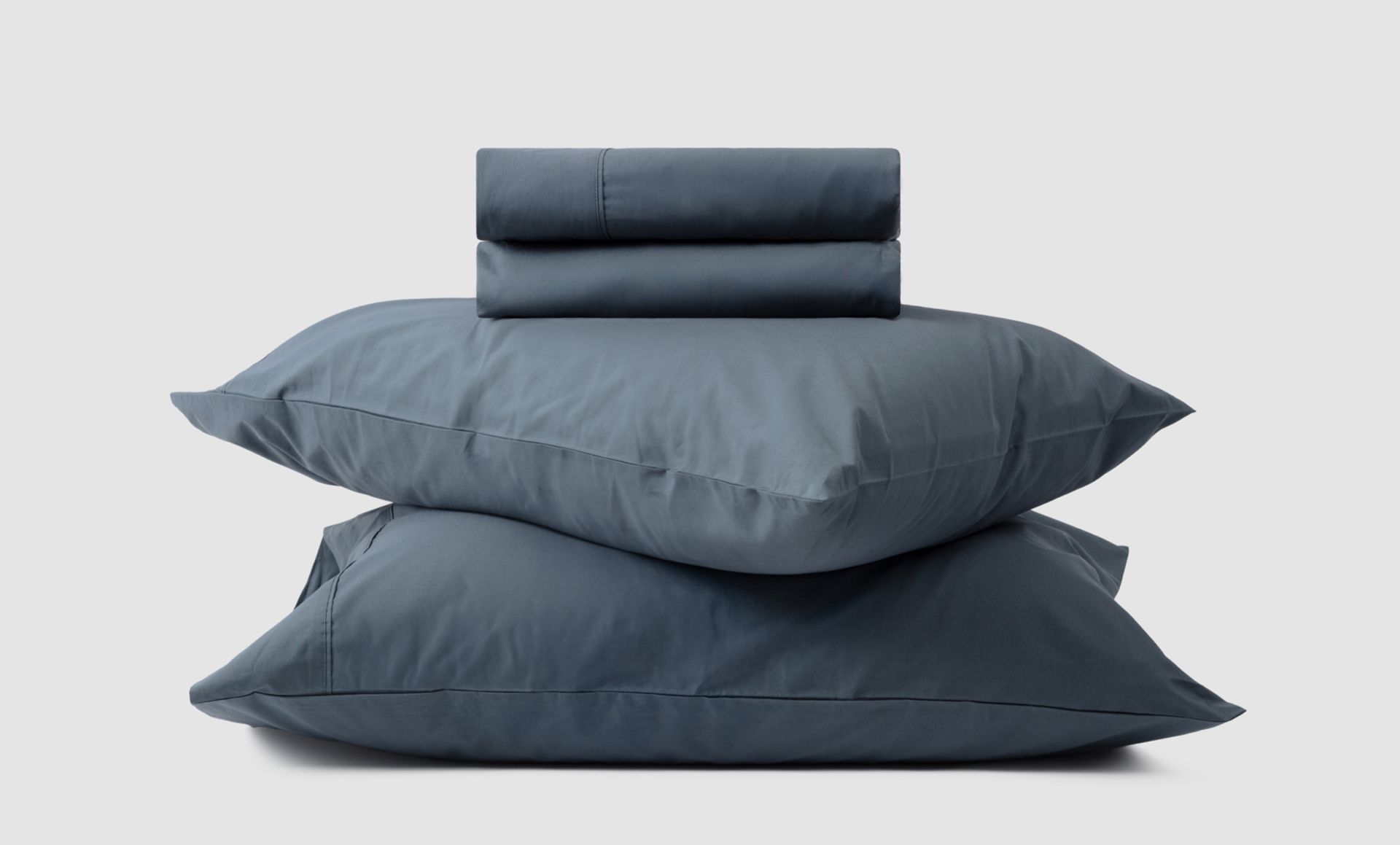 2 pillows stacked on top of each other, with a folded sheet resting on top, all of them are a dark blue colour