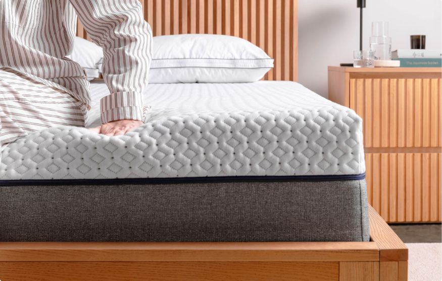 Close up of the corner of an Endy Mattress, a person in striped pajamas sits on the edge half out of frame