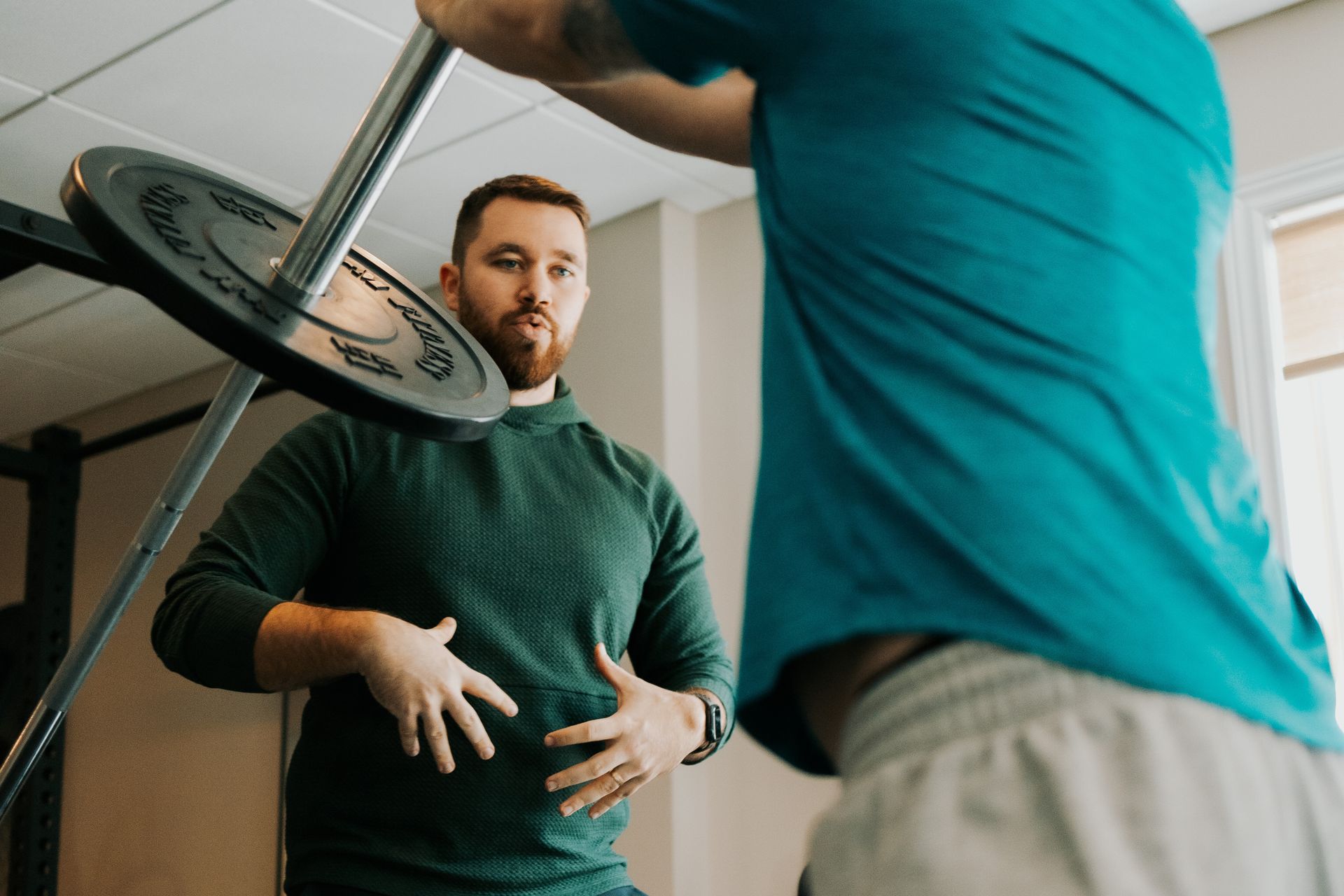 Spencer coaching a client lifting weights, gesturing towards his core muscles