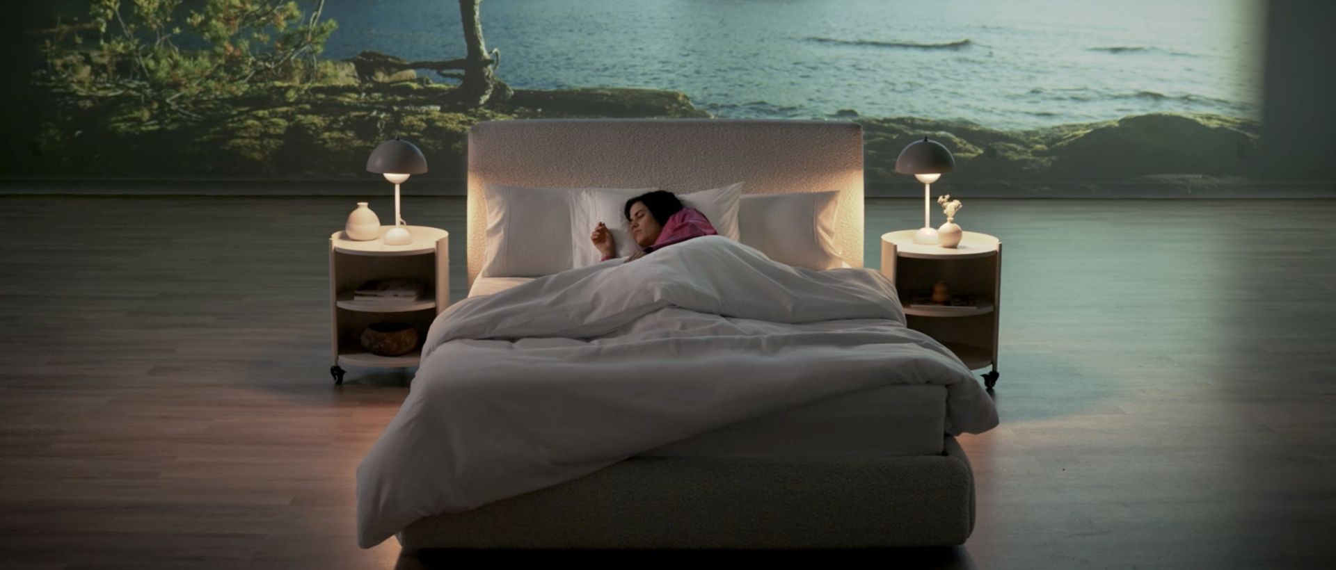 Woman in sleeping on an Endy Mattress in front of a projector screen showing a lake with trees