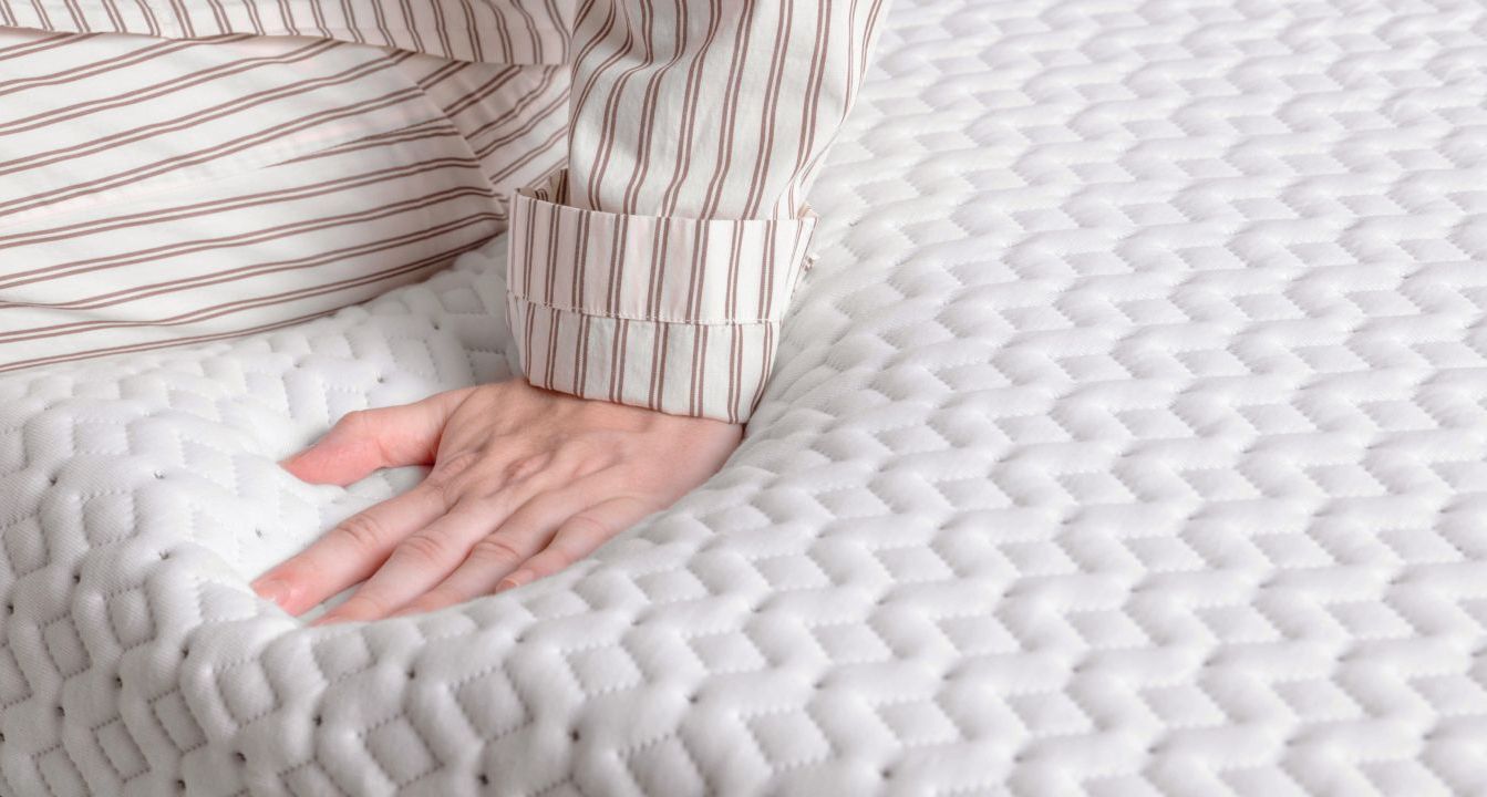 Close up of the surface of an Endy mattress, a person in striped pajamas is sitting on it and compressing it with their hand.