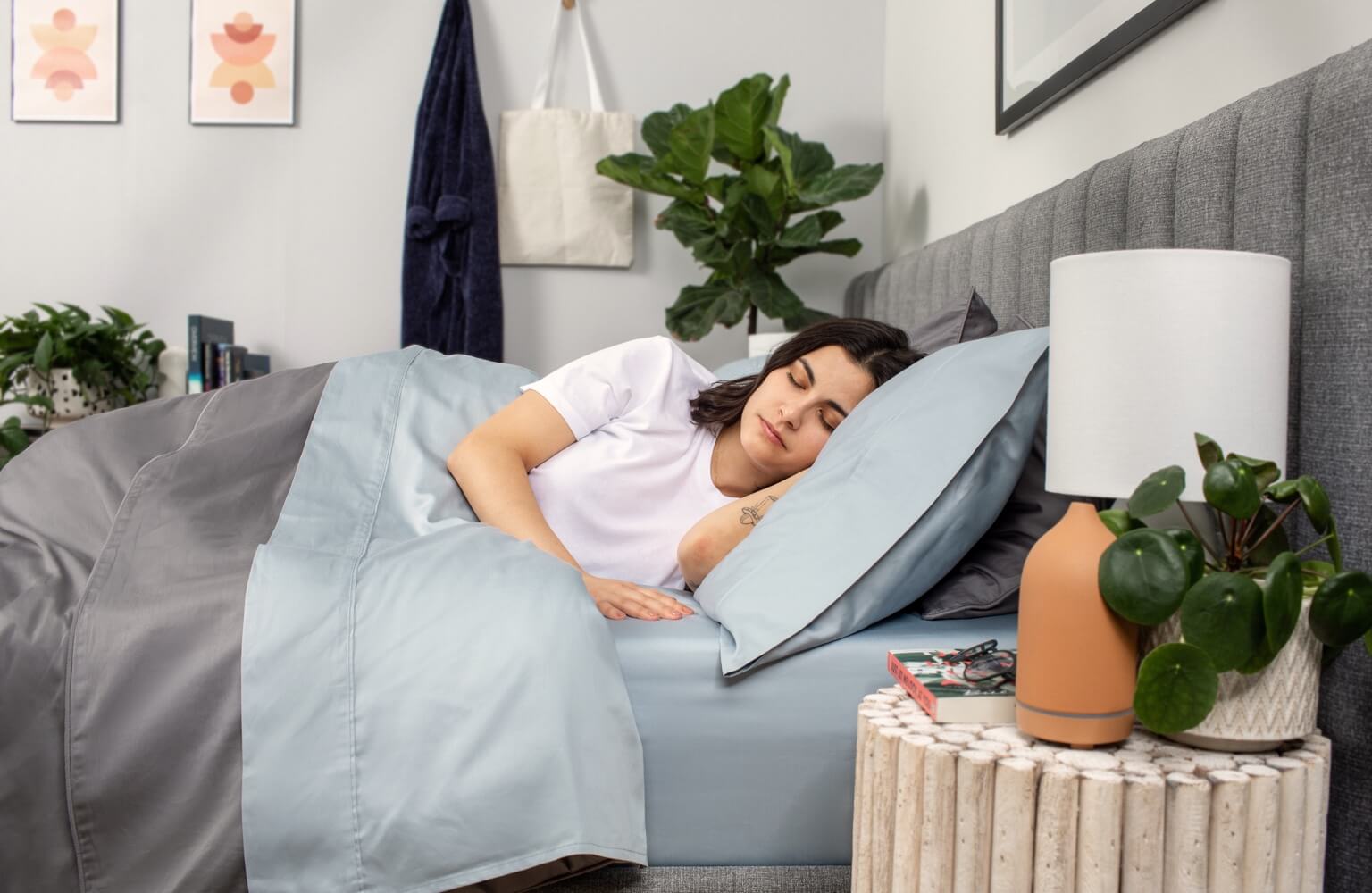 Woman sleeping in a bed with blue sheets, grey duvet cover and headboard
