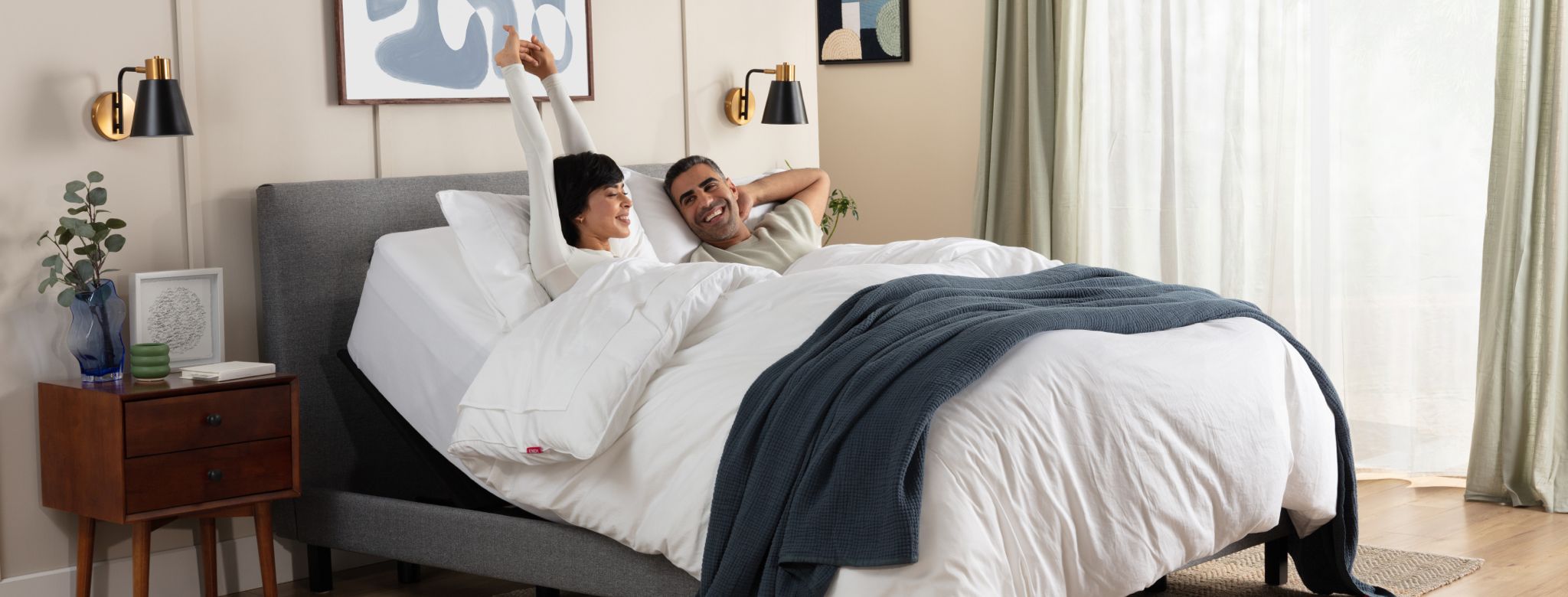 Man and woman lying on an inclined adjustable bed under a plush white Duvet, the woman is stretching her arms above her head