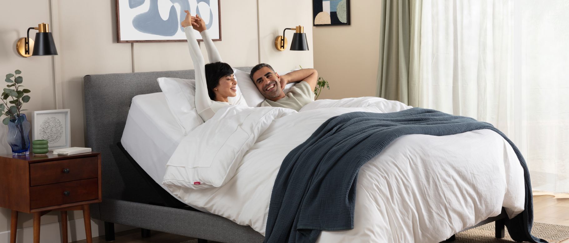 Man and woman lying on an inclined adjustable bed under a plush white Duvet, the woman is stretching her arms above her head