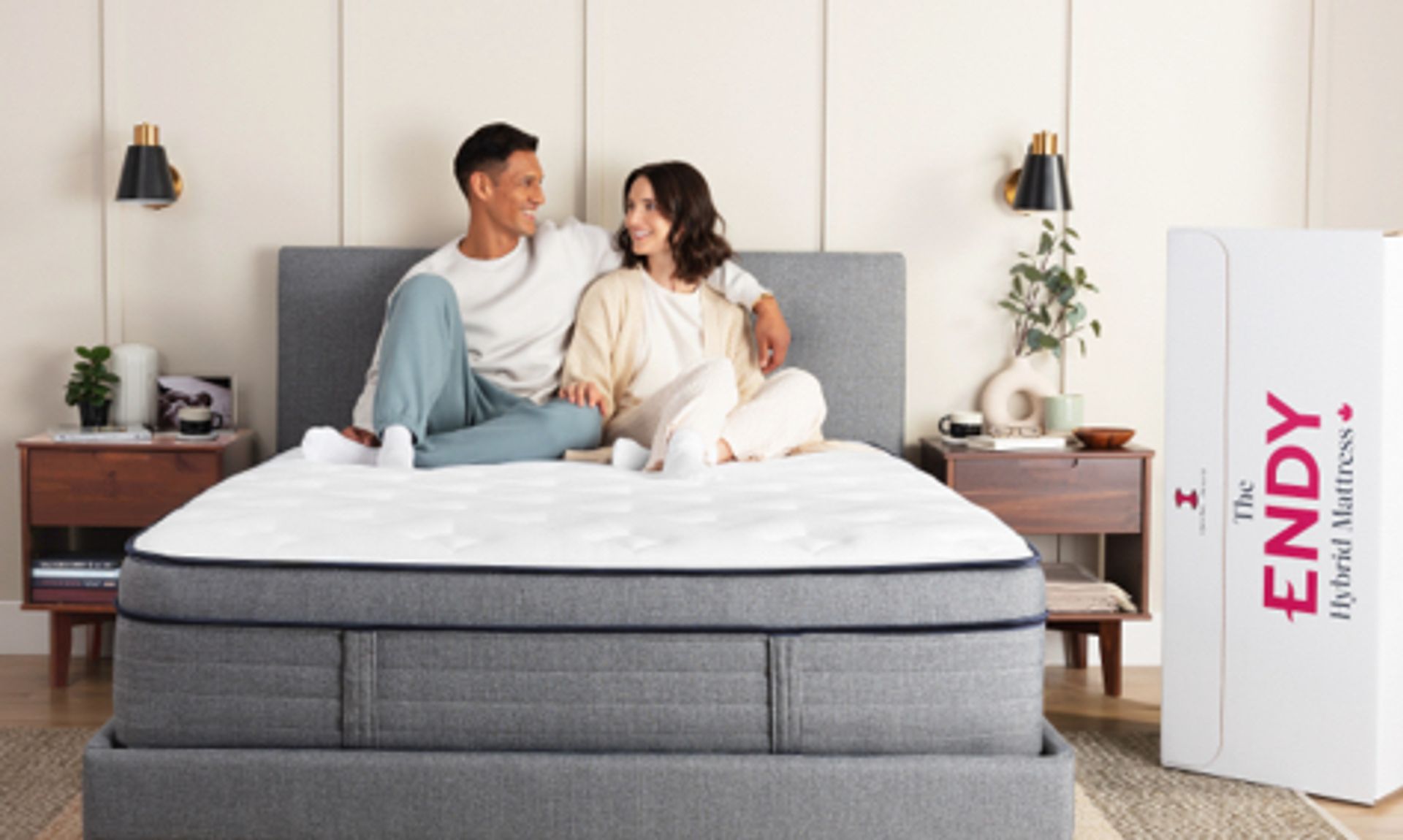 Man and woman sit on an Endy Hybrid mattress on a grey bed frame in a bedroom