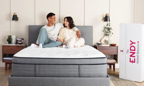 Man and woman sit on an Endy Hybrid mattress on a grey bed frame in a bedroom