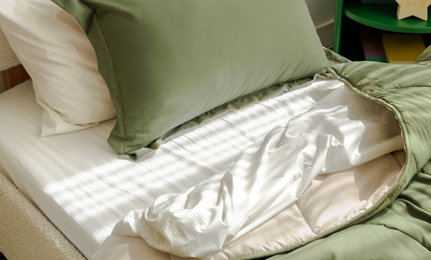 A comfy bed with white sheets, green comforter, and green and white pillows on top