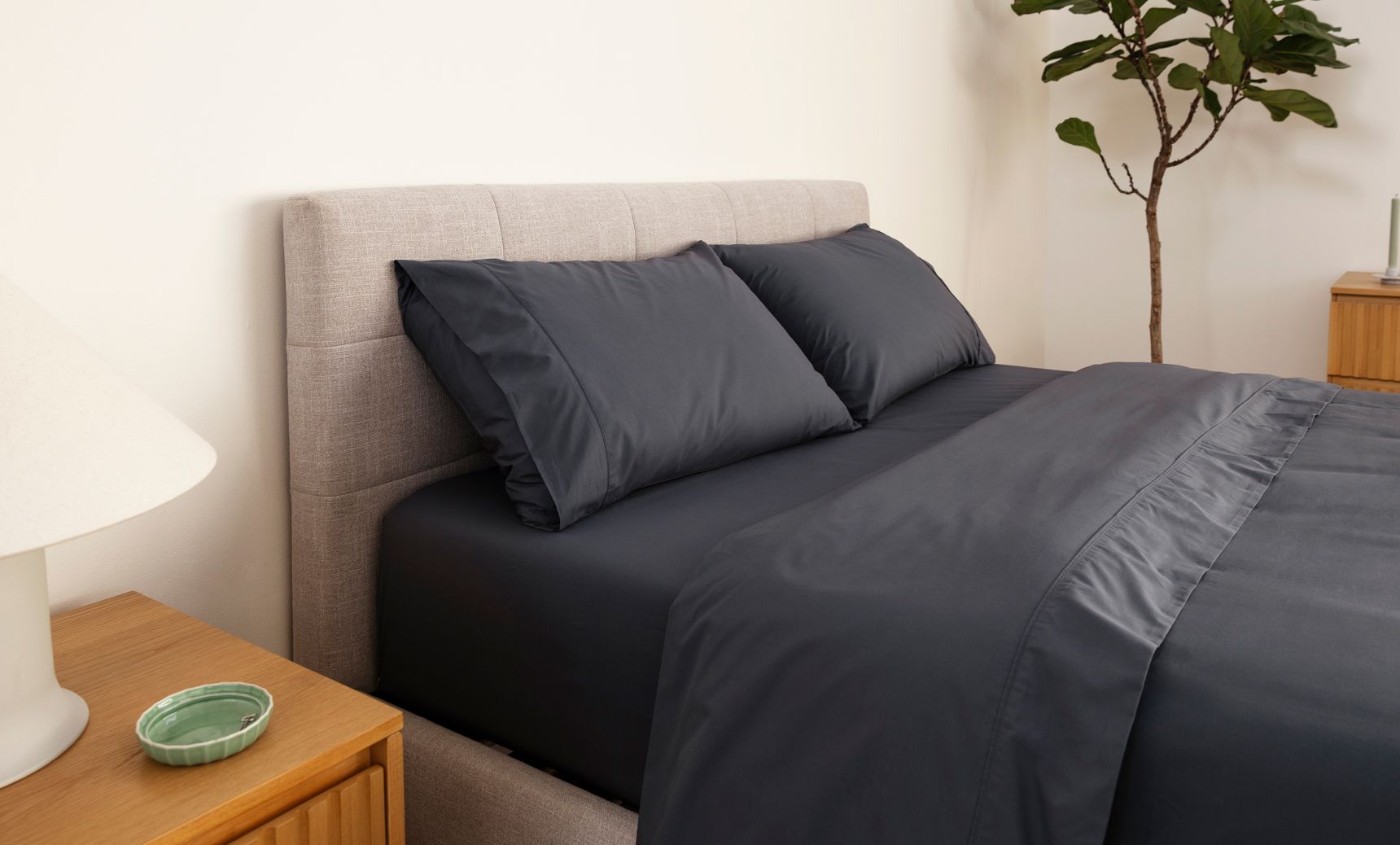 Tufted upholstered bed frame in ash grey equipped with midnight nave bedding.
