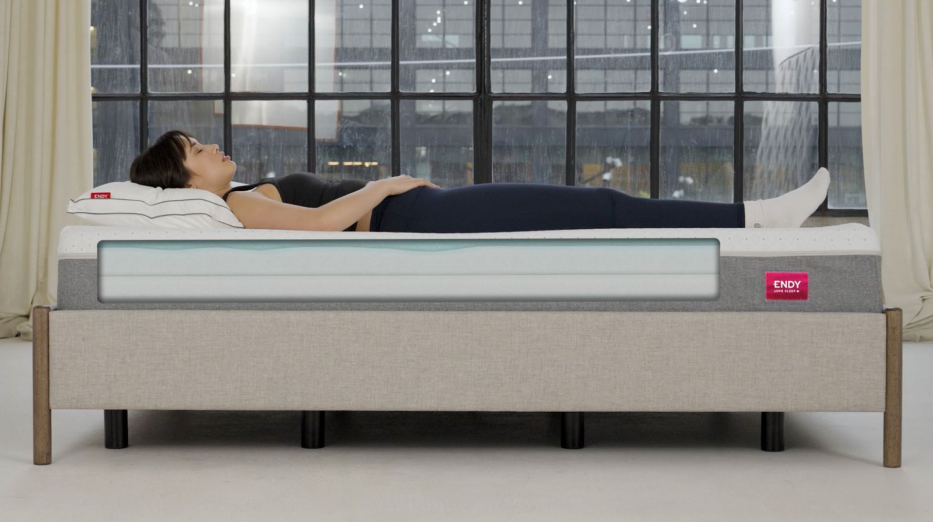 Woman is lying on her back on the Endy Mattress, a cross-section illustration shows the layers inside the mattress