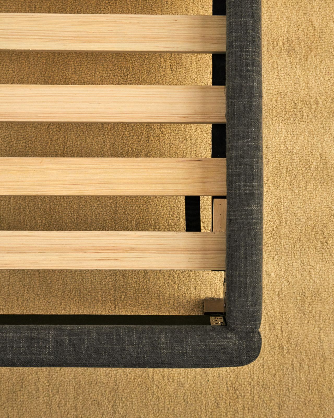 Close-up of the channel upholstered bed frame in graphite colourway with wooden slats on a carpeted floor.