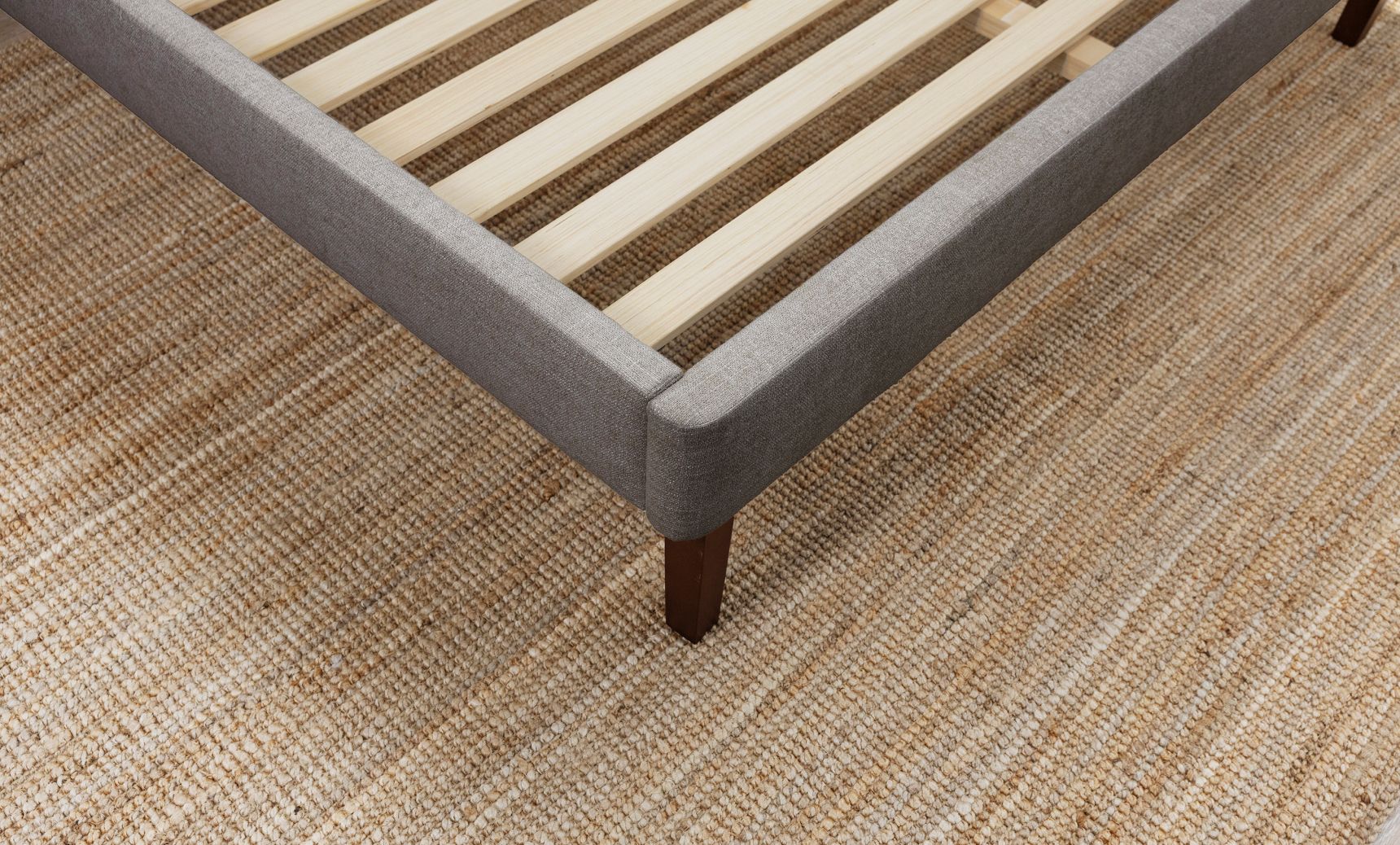 Close-up of the channel upholstered bed frame in graphite colourway with wooden slats on a carpeted floor.