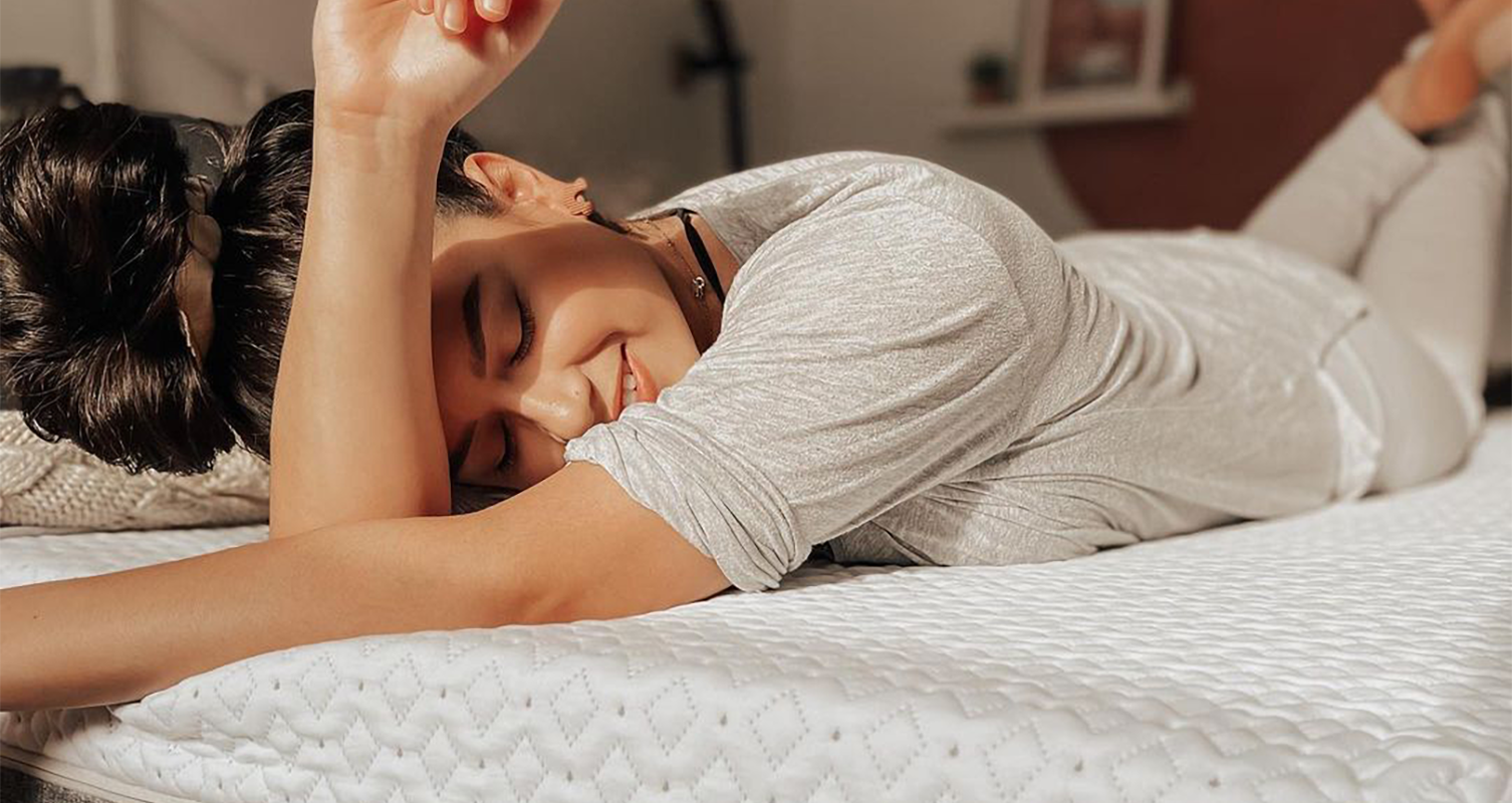 A woman lying on her stomach on an Endy Mattress, shielding her eyes from the sun with her arm