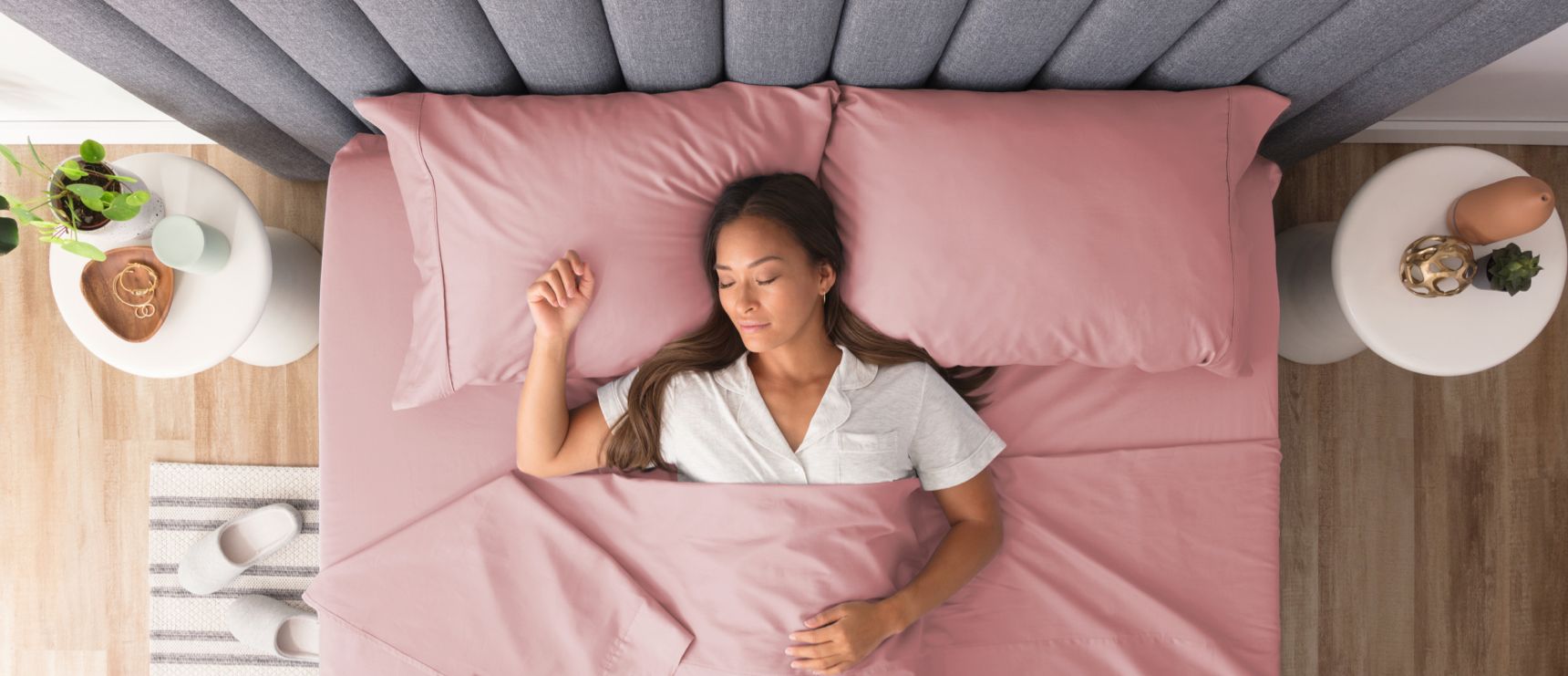 Woman lying in a bed with pink sheets and a grey headboard