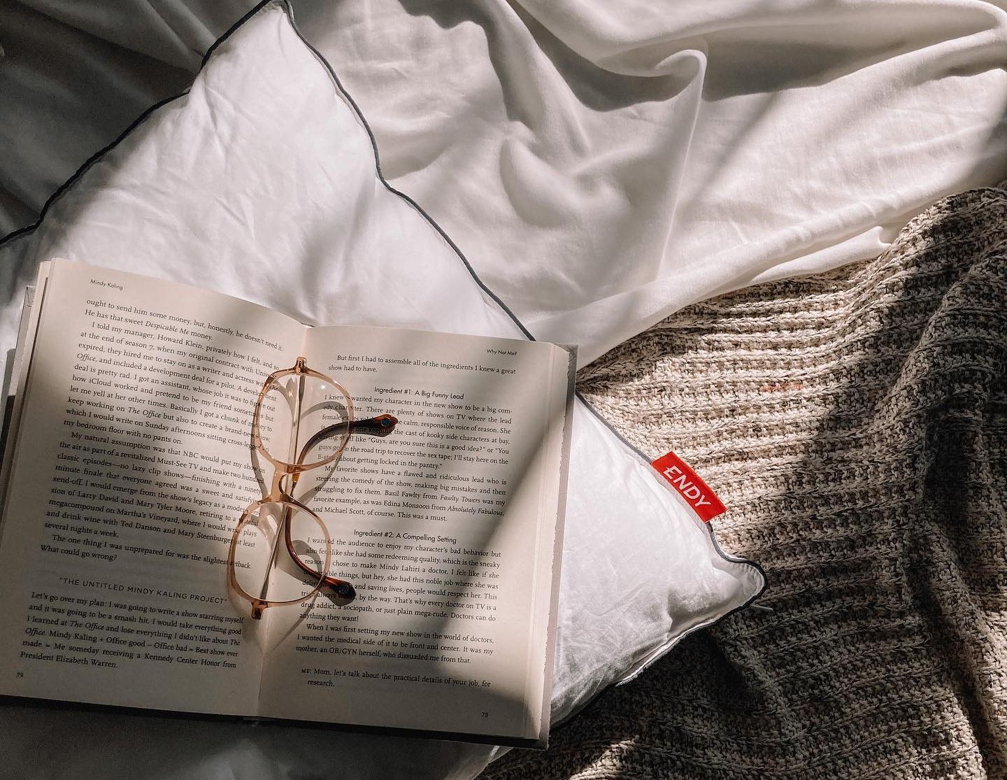 An open book resting on an Endy Customizable Pillow with glasses sitting on top of the book.