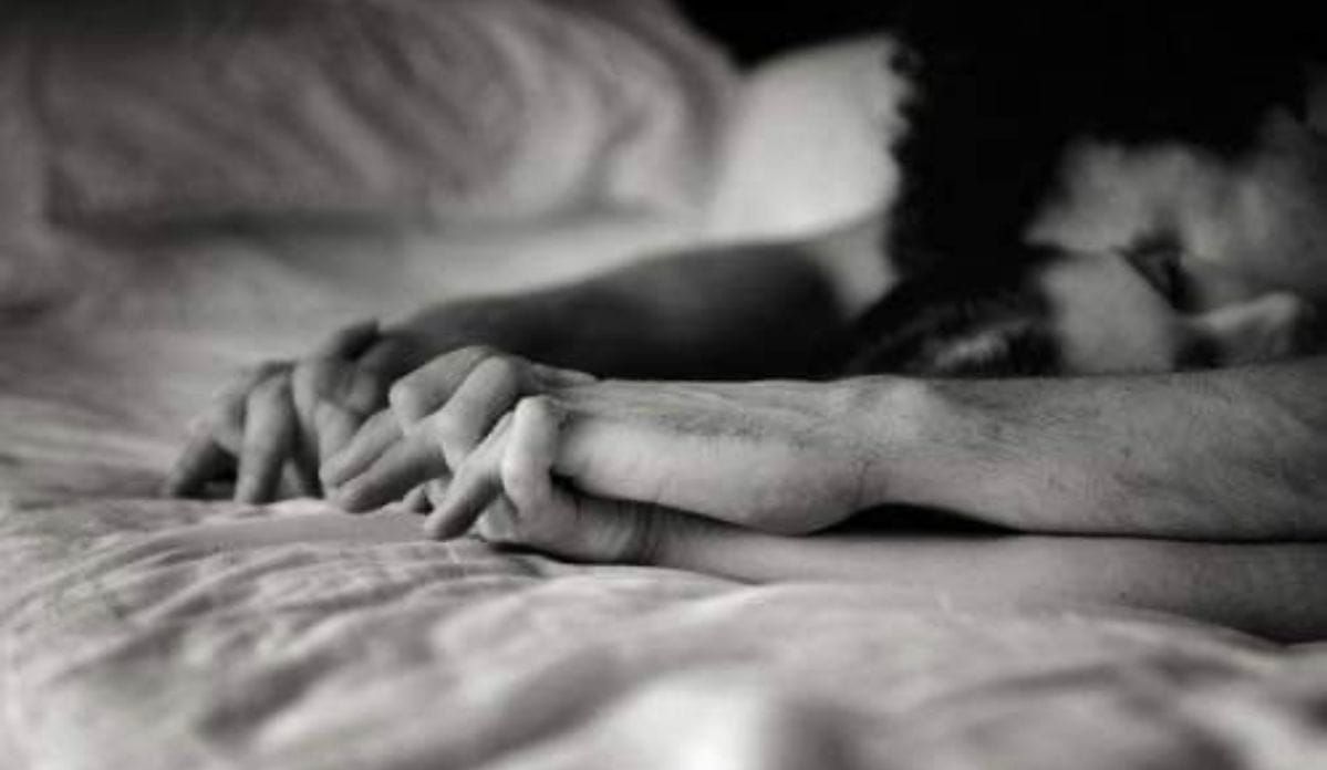 A couple's hands intertwined on white sheets