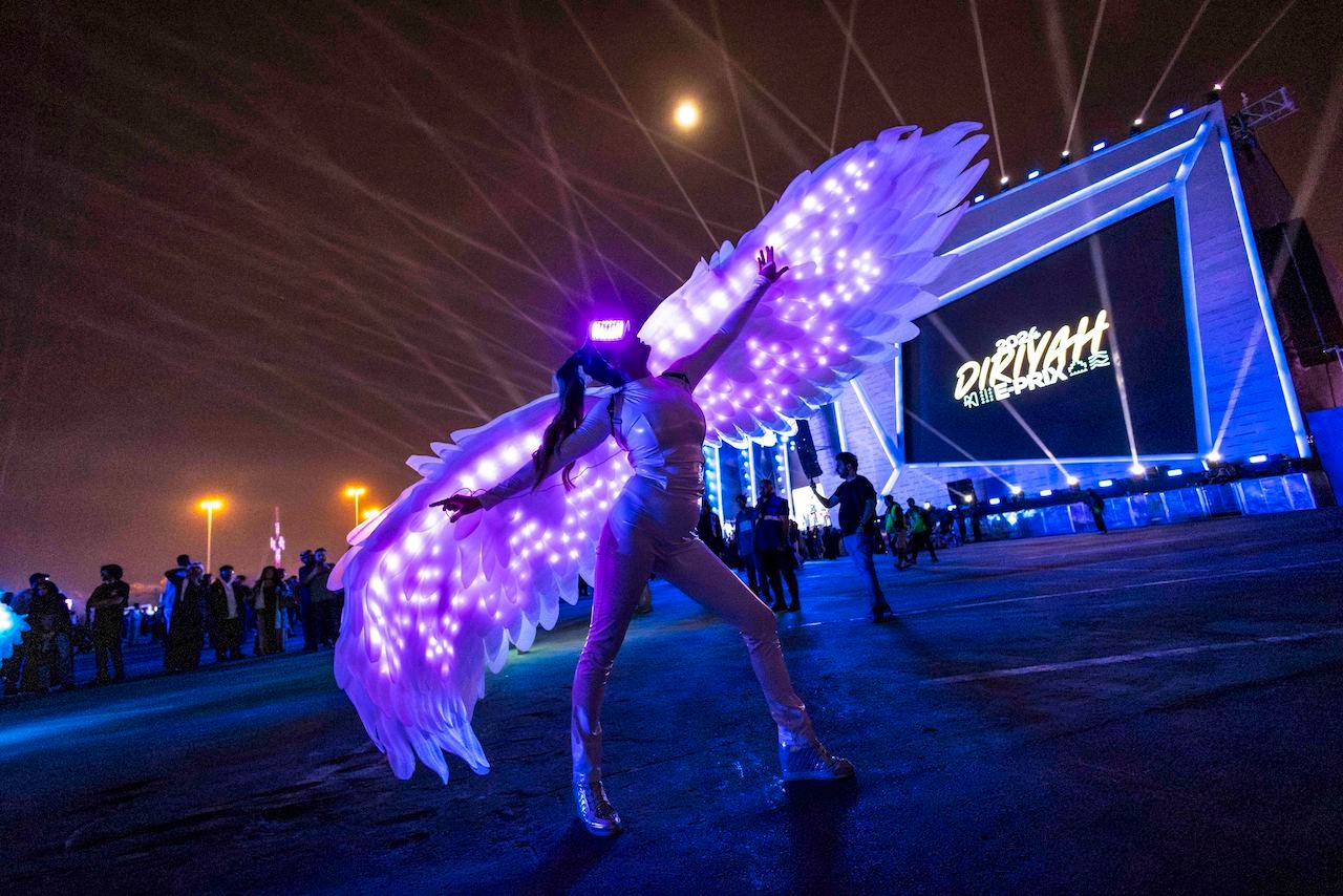 Woman wearing large white light up wings while posing in front of stage