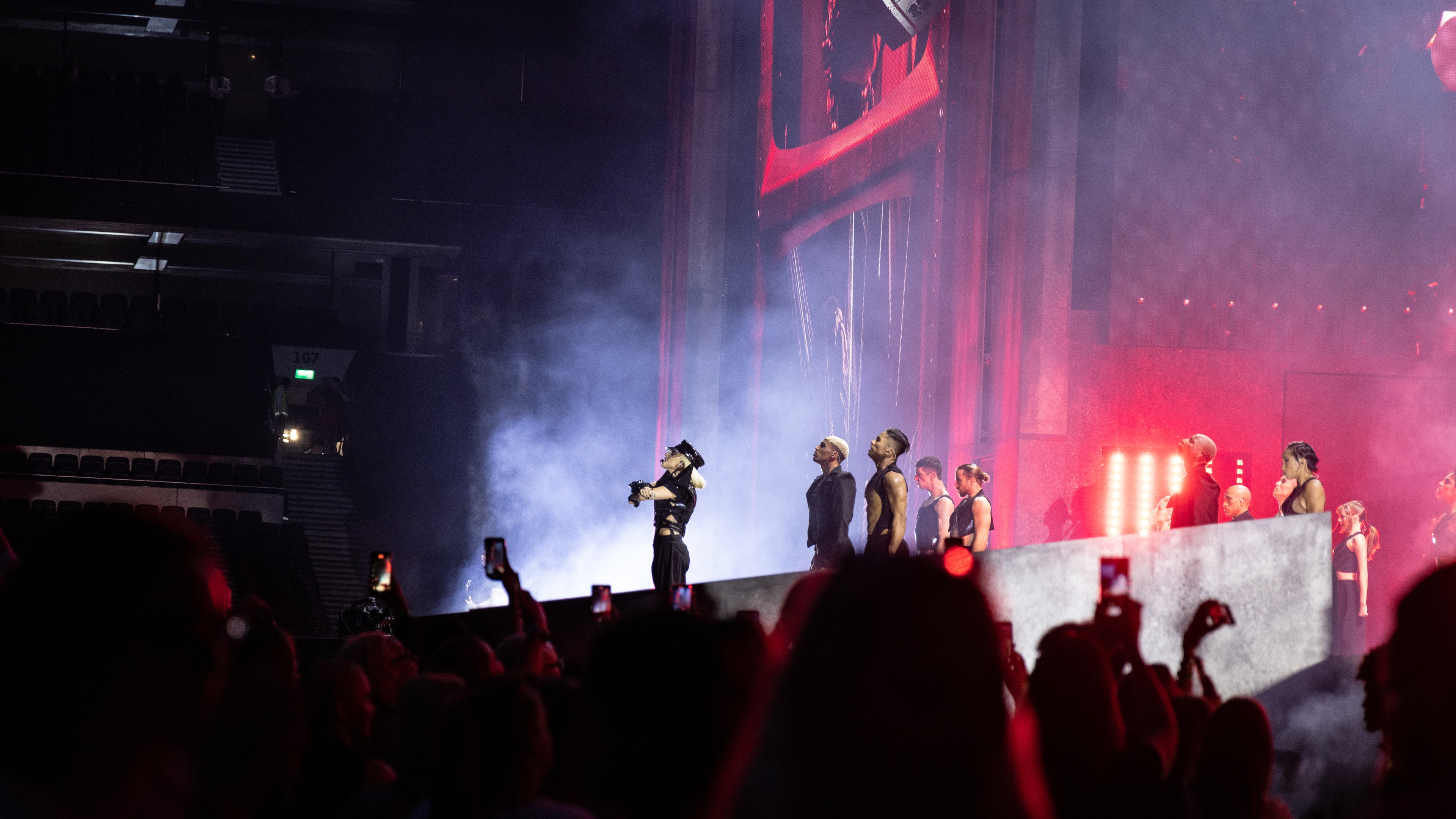 Singer Lady Gaga performing dance routine with backing dancers on stage with red lighting and smoke