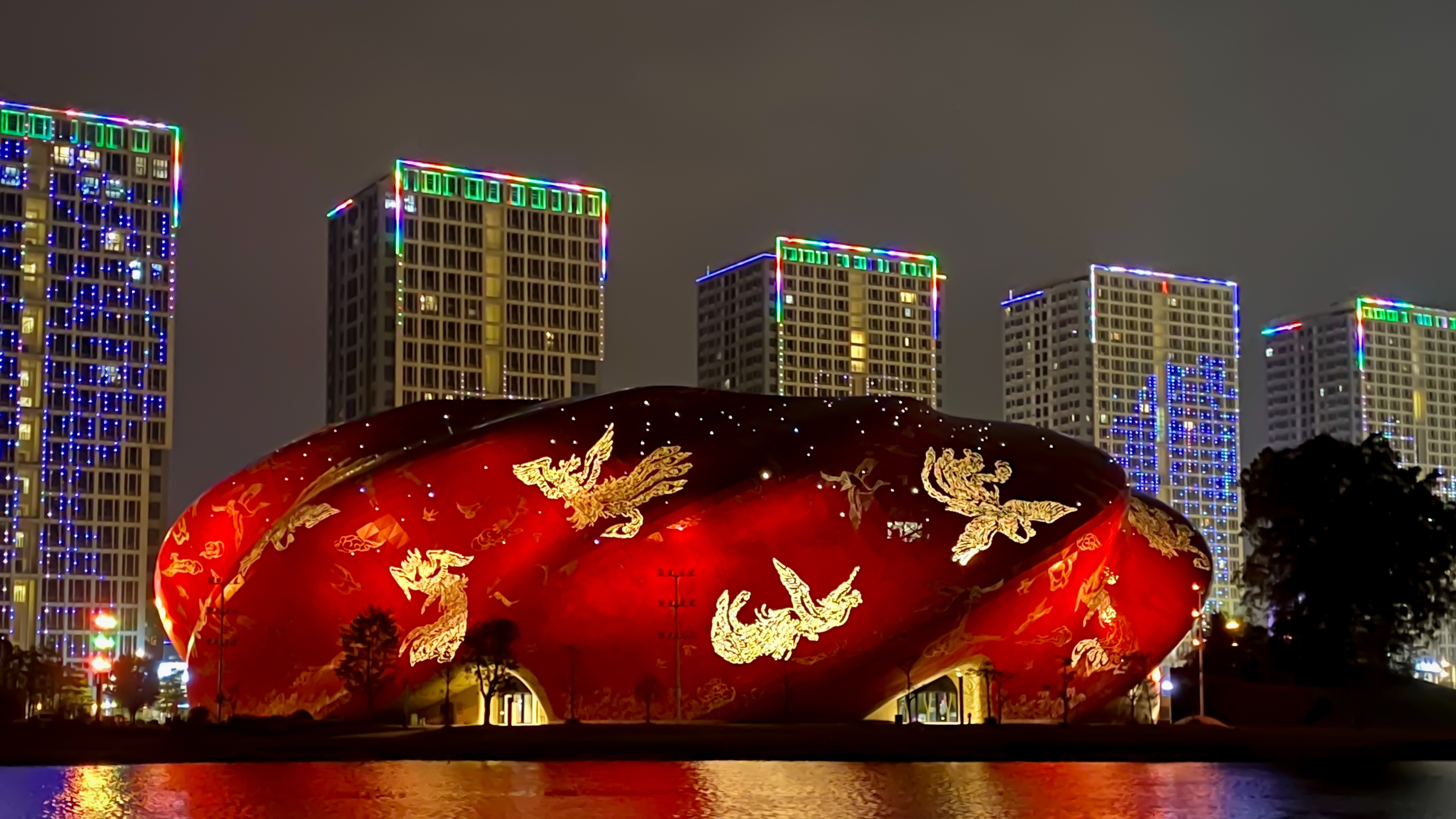 Guangzhou Grand Theatre at night light up in red and gold in front of high rise buildings
