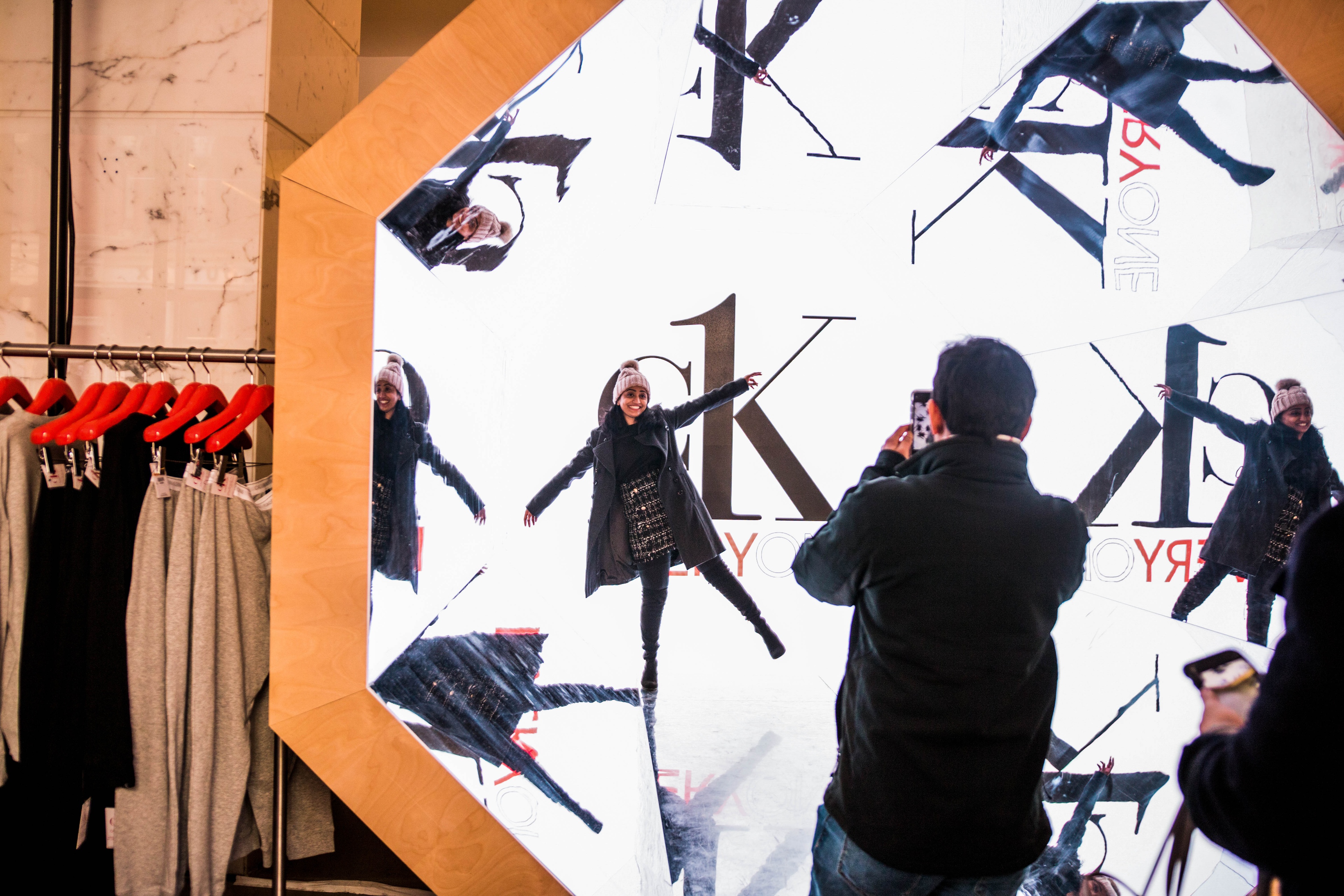 Woman in coat and beanie posting in front of CK photo booth