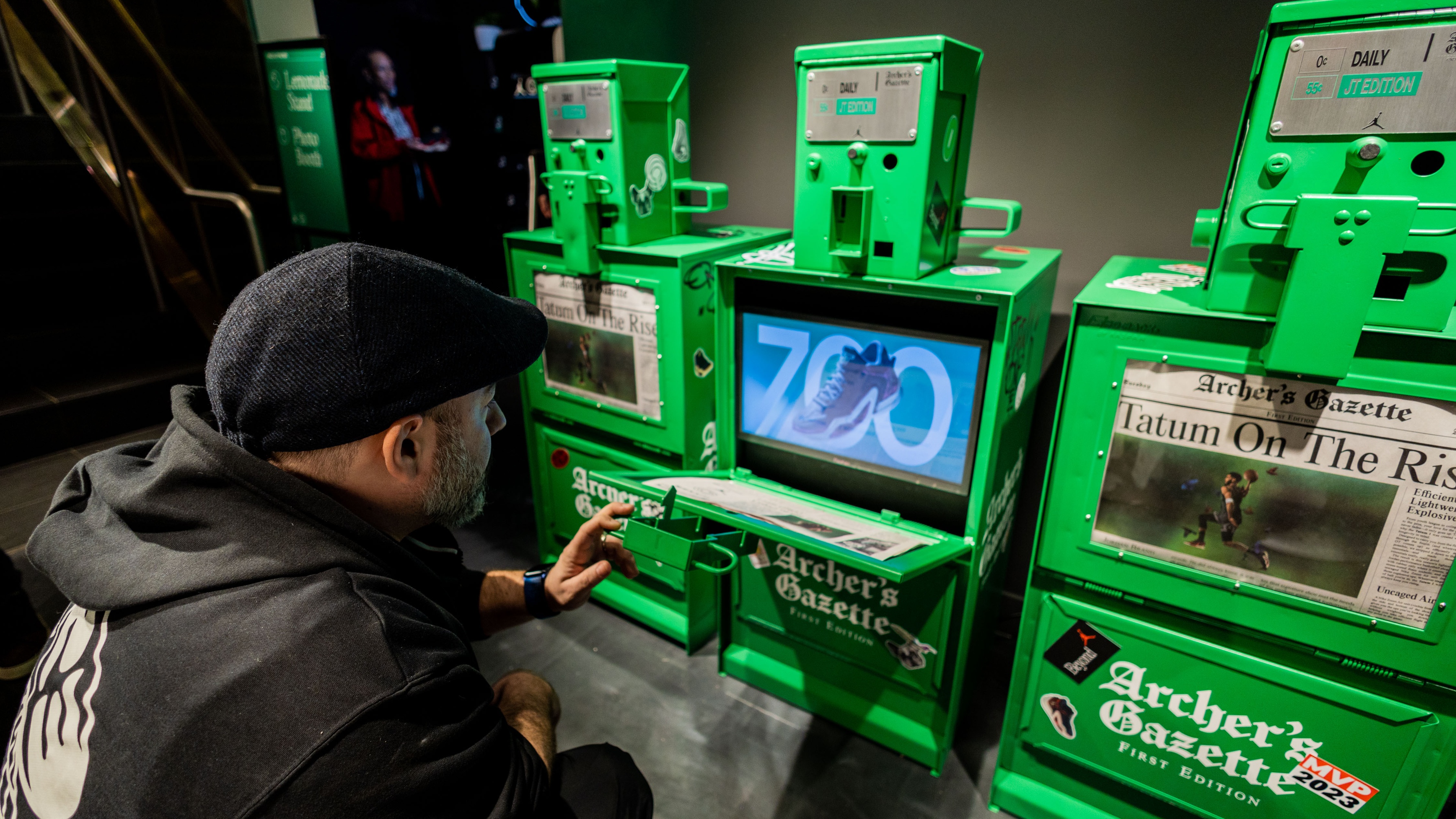 person interacting with vintage newspaper dispenser fitted with screen displaying Nike brand products