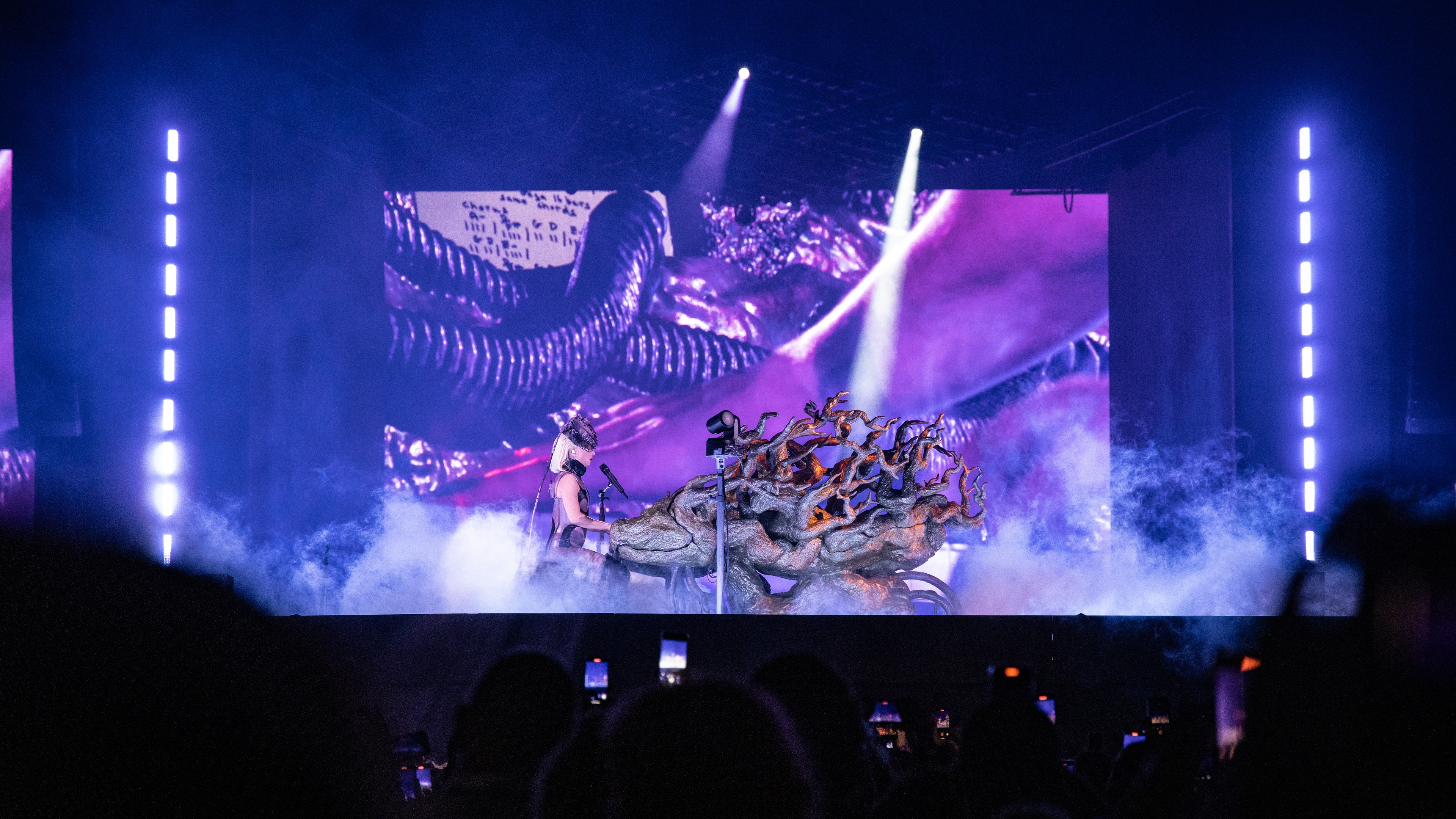 Singer Lady Gaga performing on a piano with tree prop and LED screen