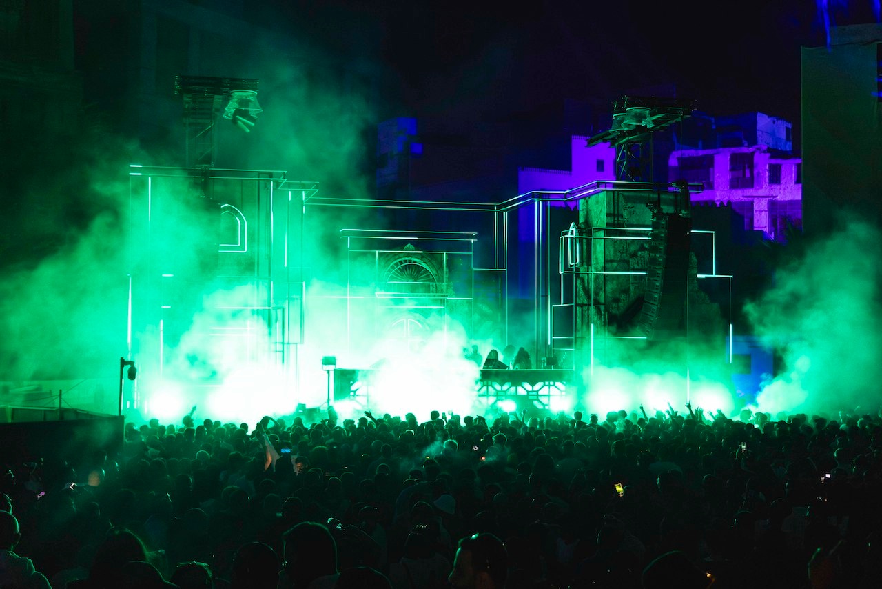 DJs on outdoor stage with green lights and haze